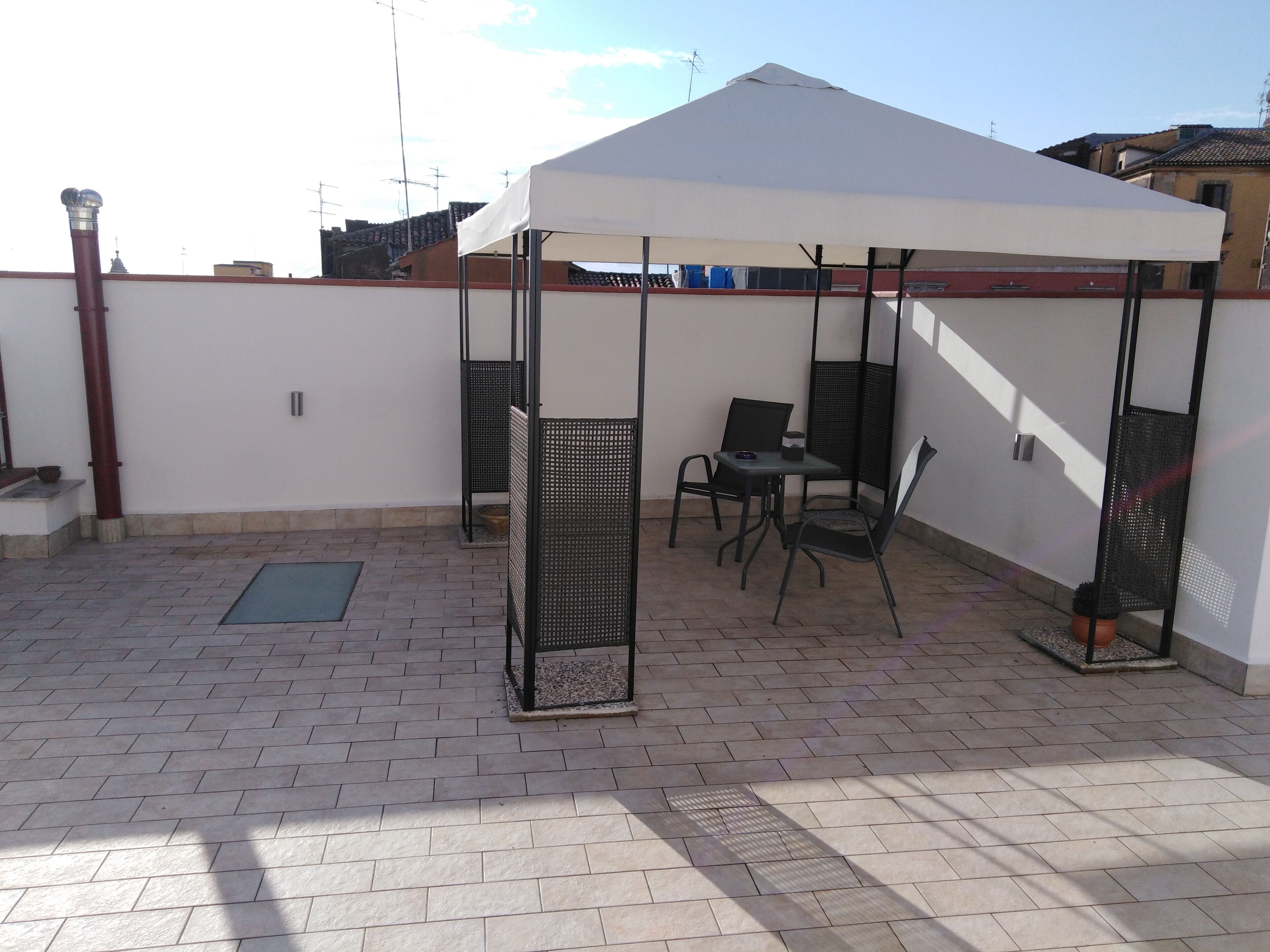 Une terrasse sur le toit, dotée d’un auvent blanc, de deux chaises en métal, d’une petite table et d’une plante en pot.