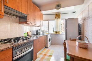 Uma cozinha com armários de madeira, fogão a gás, máquina de lavar roupa e uma mesa de jantar com cadeiras.