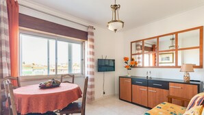 Ein Zimmer mit Esstisch, Stühlen, einer Sitzecke, einem Fernseher, einem Schrank und einem Fenster mit Vorhängen.