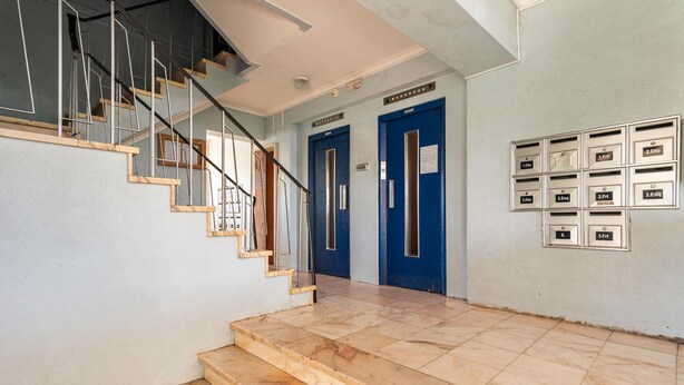 Eine Treppe führt zu einer Zwischenebene mit einer blauen Tür und Briefkästen an der Wand.
