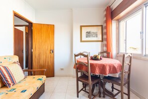 Um quarto aconchegante com porta de madeira, um sofá com almofadas estampadas, uma mesa de jantar com toalha vermelha e um quadro na parede.