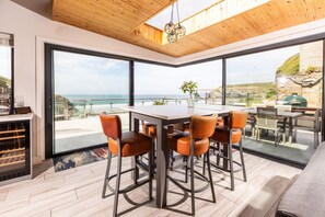 Zona pranzo moderna con un tavolo grande e sedie, ampie finestre con vista sull'oceano e soffitto in legno.