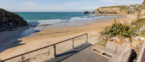 Una playa con una terraza de madera y un espacio de descanso con cojines.