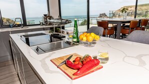 A modern kitchen with a large island, a view of the ocean, and a dining area with chairs and a table.