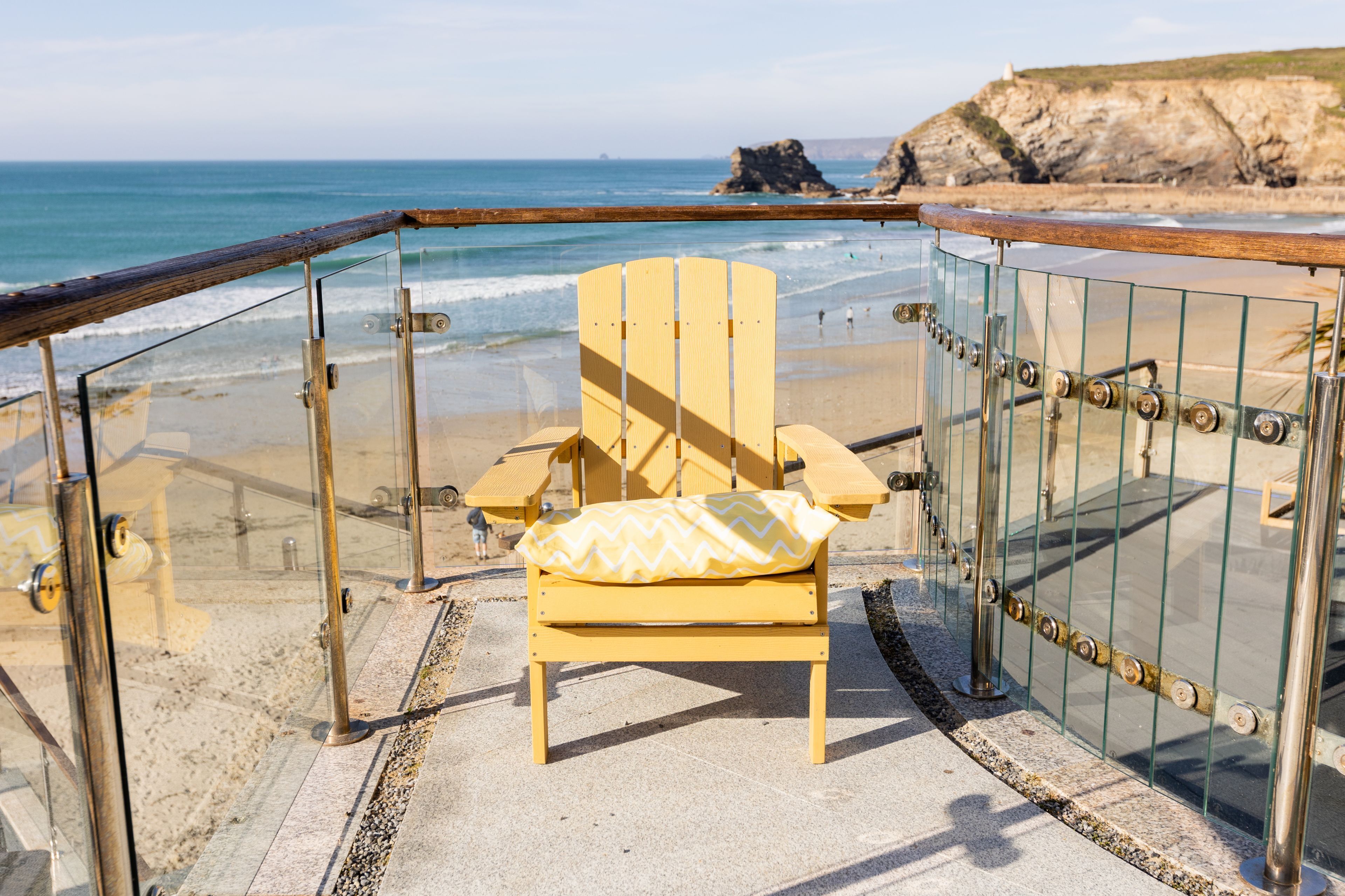 A beach chair with a cushion, a glass railing, and a view of the ocean and cliffs.
