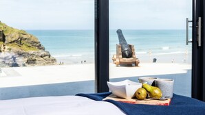 A room with a bed, a view of the beach, a statue, and some fruit.