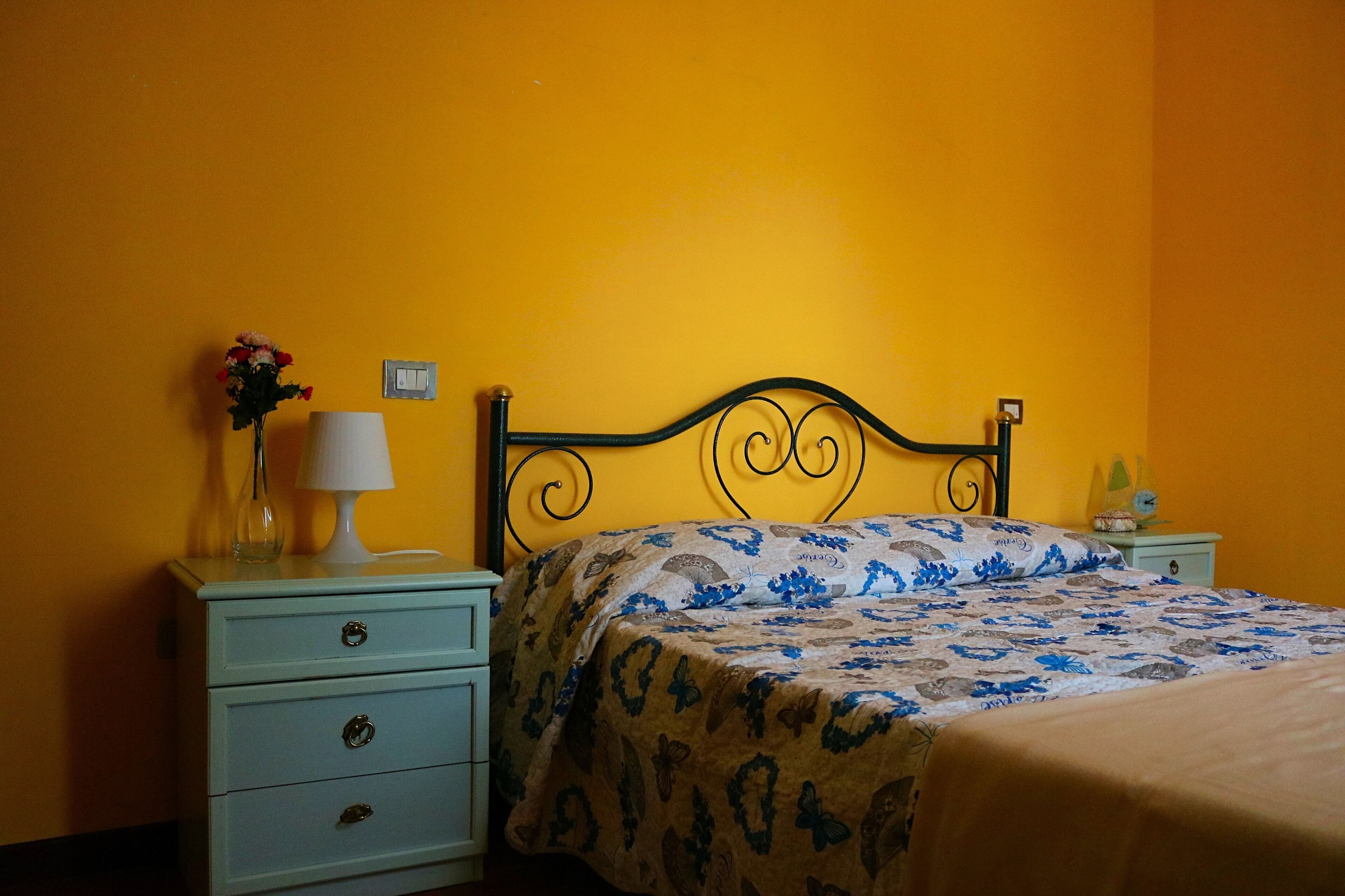A bed with a patterned bedspread, a bedside table with a lamp, and a vase with flowers.