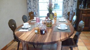 A round wooden dining table with chairs, set for breakfast with cups, plates, and condiments. - Chambres d'hôtes Le Bourdieu (Soulignac)