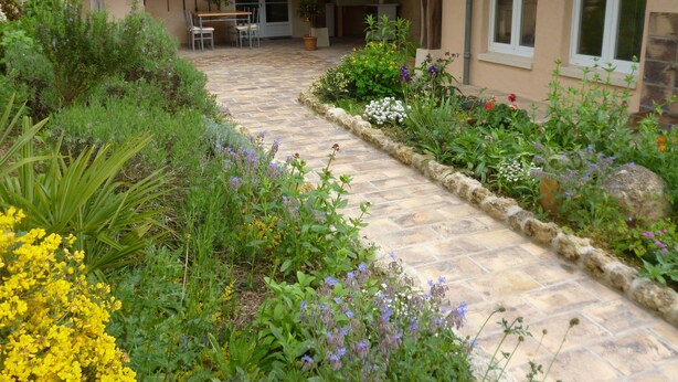A stone pathway leading to a covered patio area with outdoor seating and a variety of flowering plants. - Chambres d'hôtes Le Bourdieu (Soulignac)