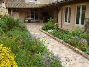 Un sendero de piedra conduce a un porche cubierto con mobiliario de exterior y una variedad de plantas en flor.