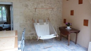 A rustic room with a stone wall, a wooden ceiling, a hanging chair, a small wooden table with a potted plant, and a window with curtains. - Chambres d'hôtes Le Bourdieu (Soulignac)