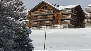 Een houten chalet met meerdere balkons, omringd door sneeuwtruiige bomen.