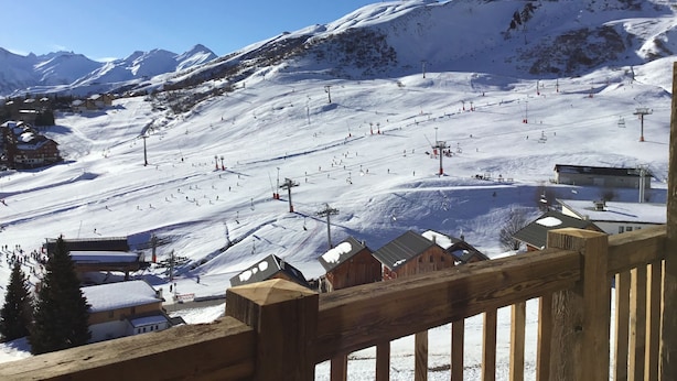 Een met sneeuw bedekte piste met skiliften en gebouwen op de achtergrond.