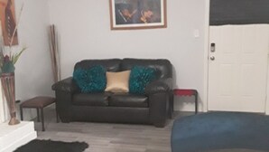 Una sala de estar con un sofá de cuero negro, un sofá azul, un cuadro enmarcado en la pared y una puerta blanca.