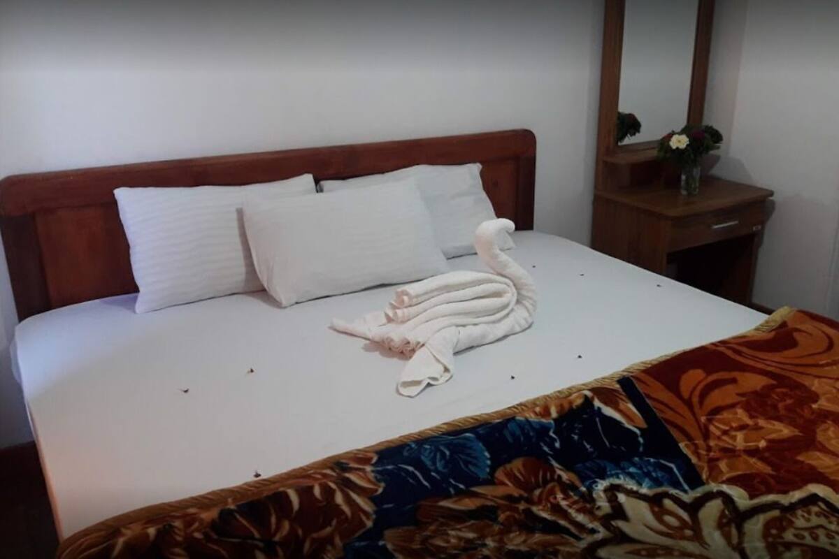 Een bed met witte lakens, een opgevouwen handdoek en een plaid met bloemenprint.