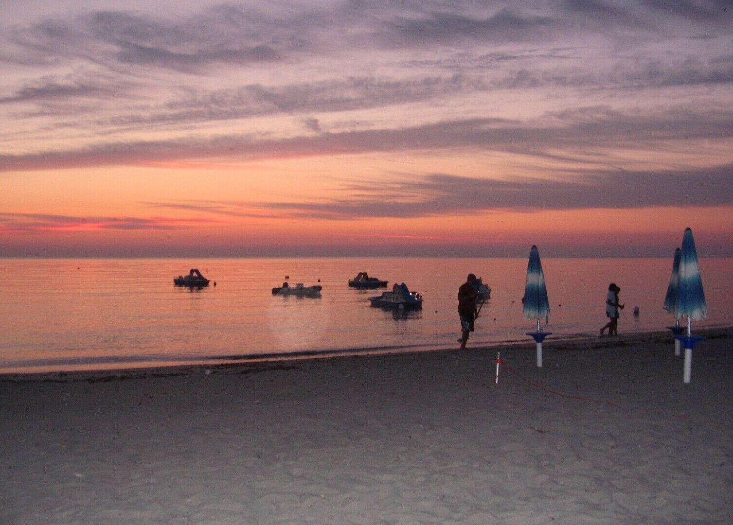 Ein Strand mit Booten, Menschen und Sonnenschirmen.