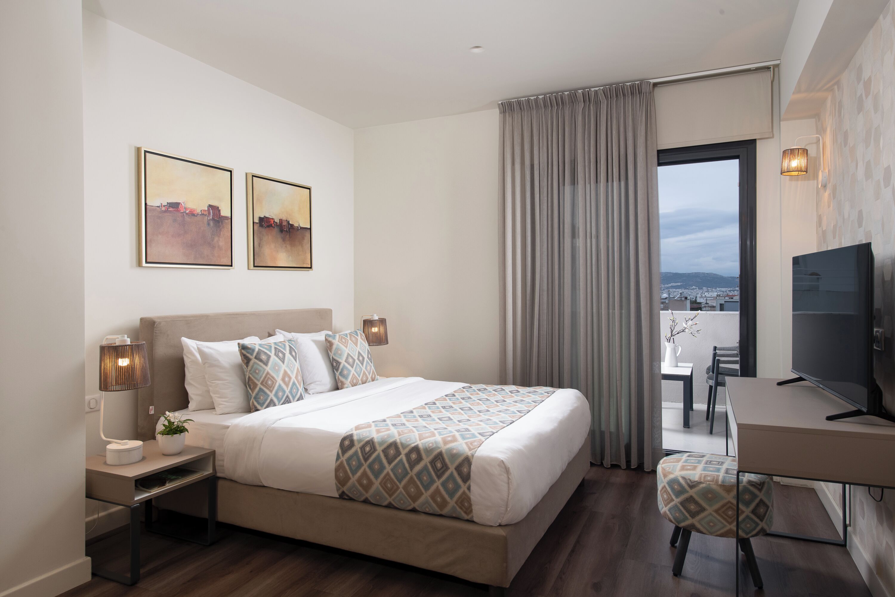 A modern hotel room with a bed, bedside tables, a desk, a television, and a balcony with a view.