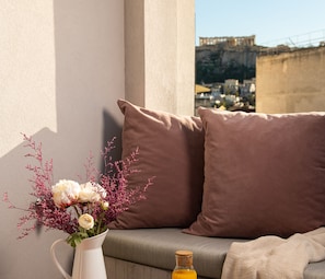 A balcony with a sofa, cushions, a vase with flowers, and a bottle.