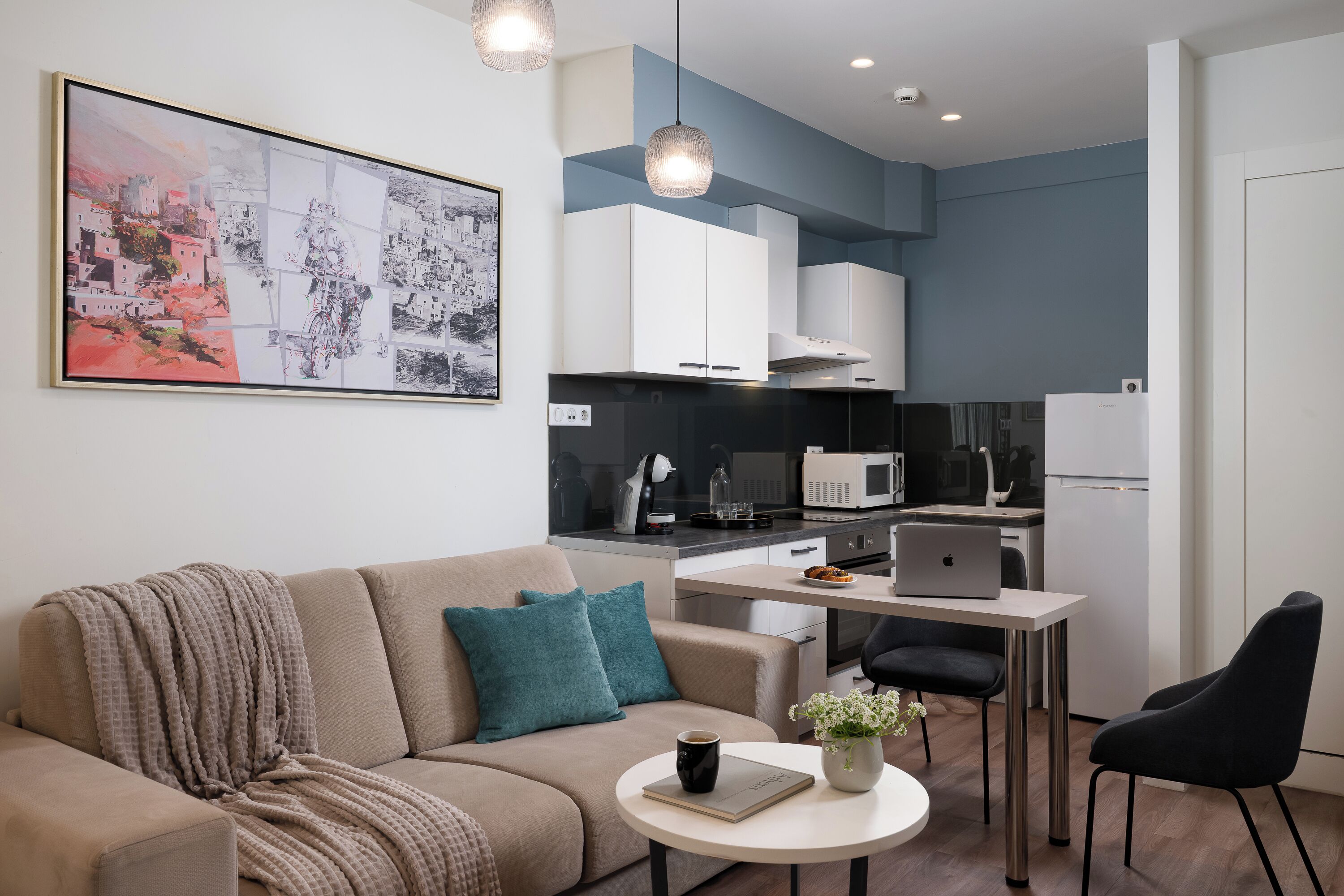 Een moderne woonkamer met een bank, salontafel en een eethoek met een laptop en een plant.