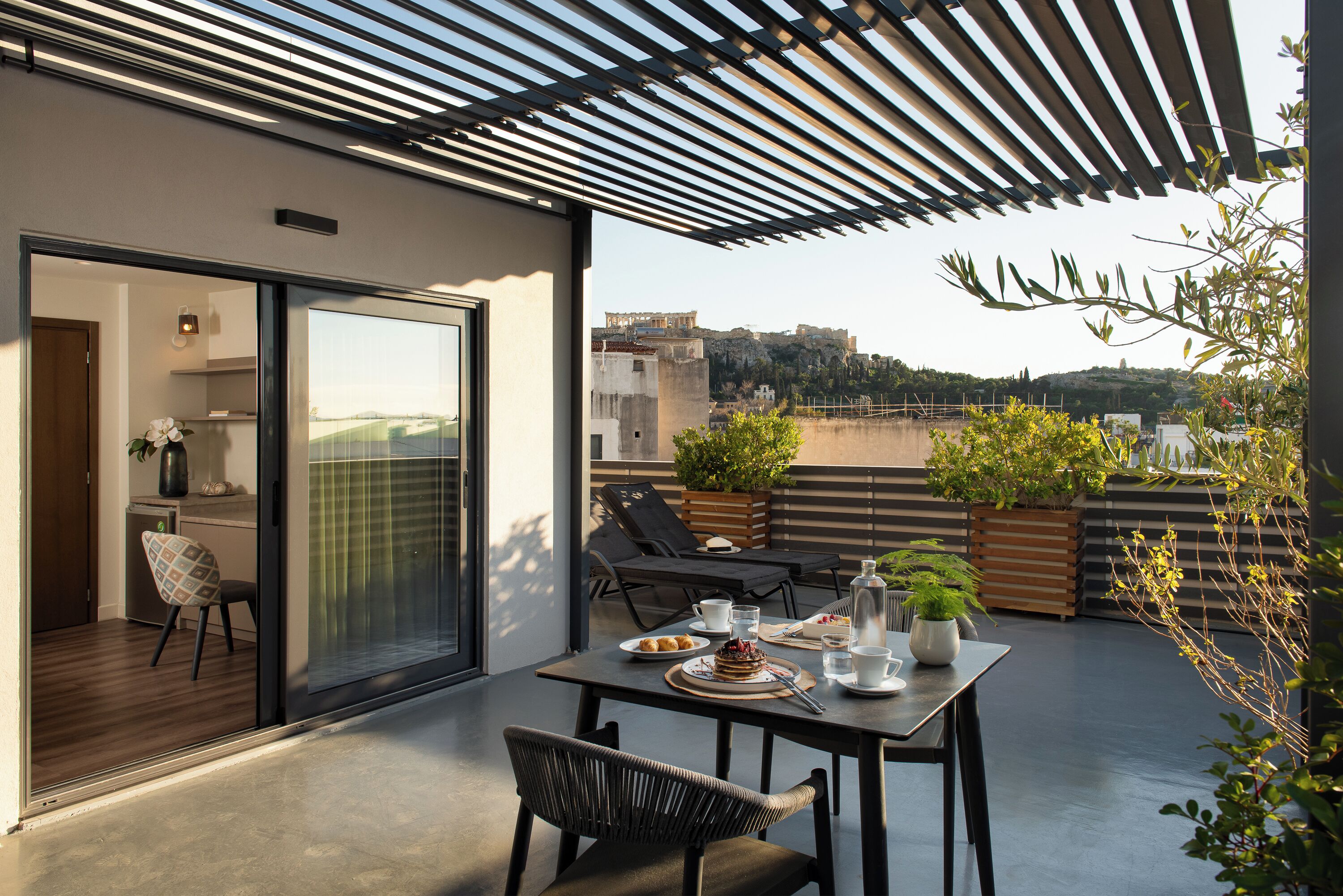 A modern outdoor dining area with a table set for two, a chair, and a view of a cityscape.