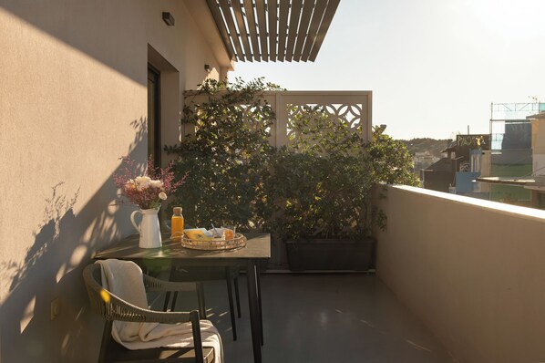 Un balcone con tavolo, sedie, una pianta in vaso e un pergolato.