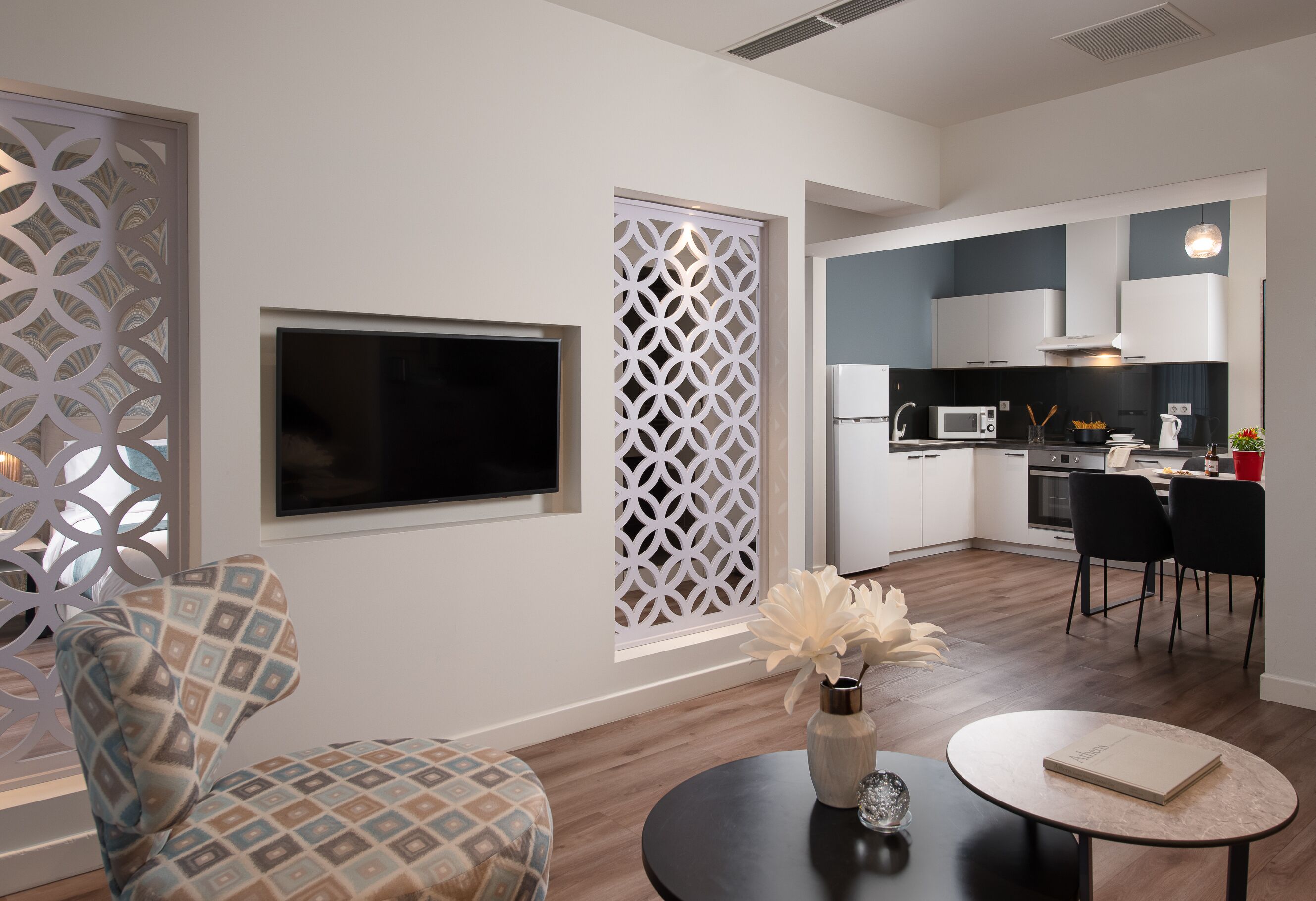 A modern living room with a TV, patterned chair, decorative vase, and a round table.