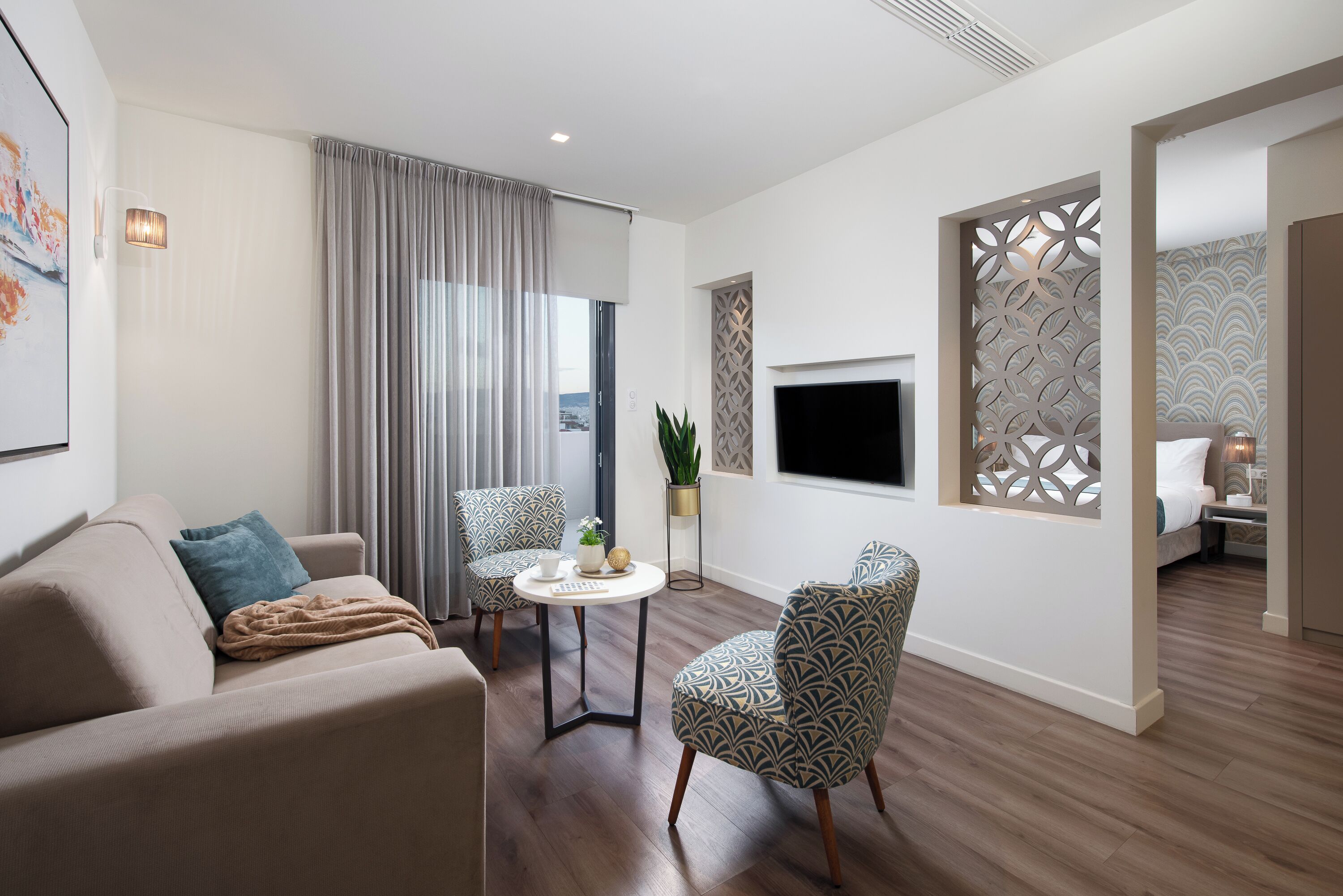 Una sala de estar moderna con un sofá, dos sillones estampados, una mesita redonda y un televisor montado en la pared.
