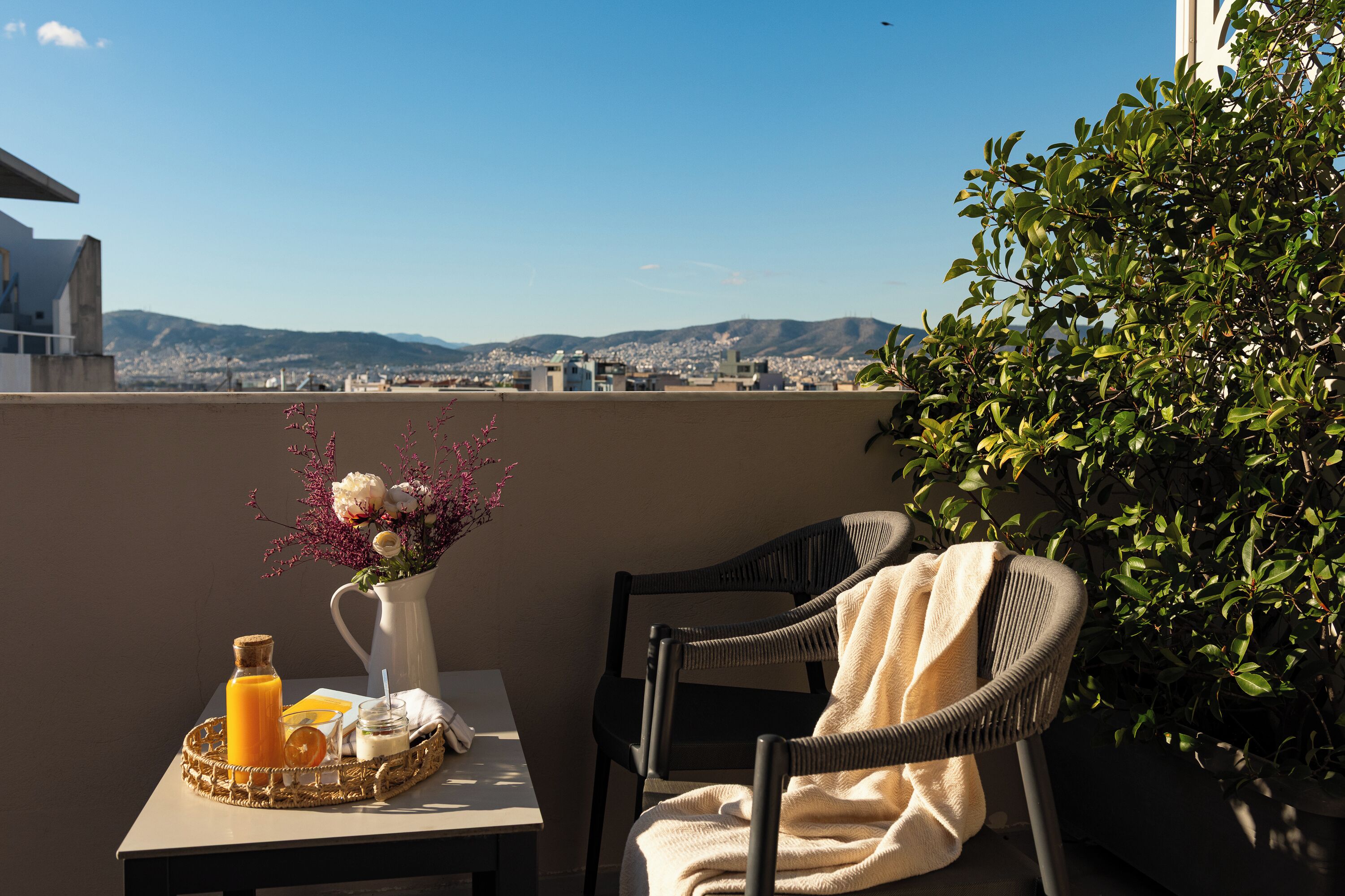 A balcony with a table, chairs, a vase with flowers, and a tray with a bottle and a glass.