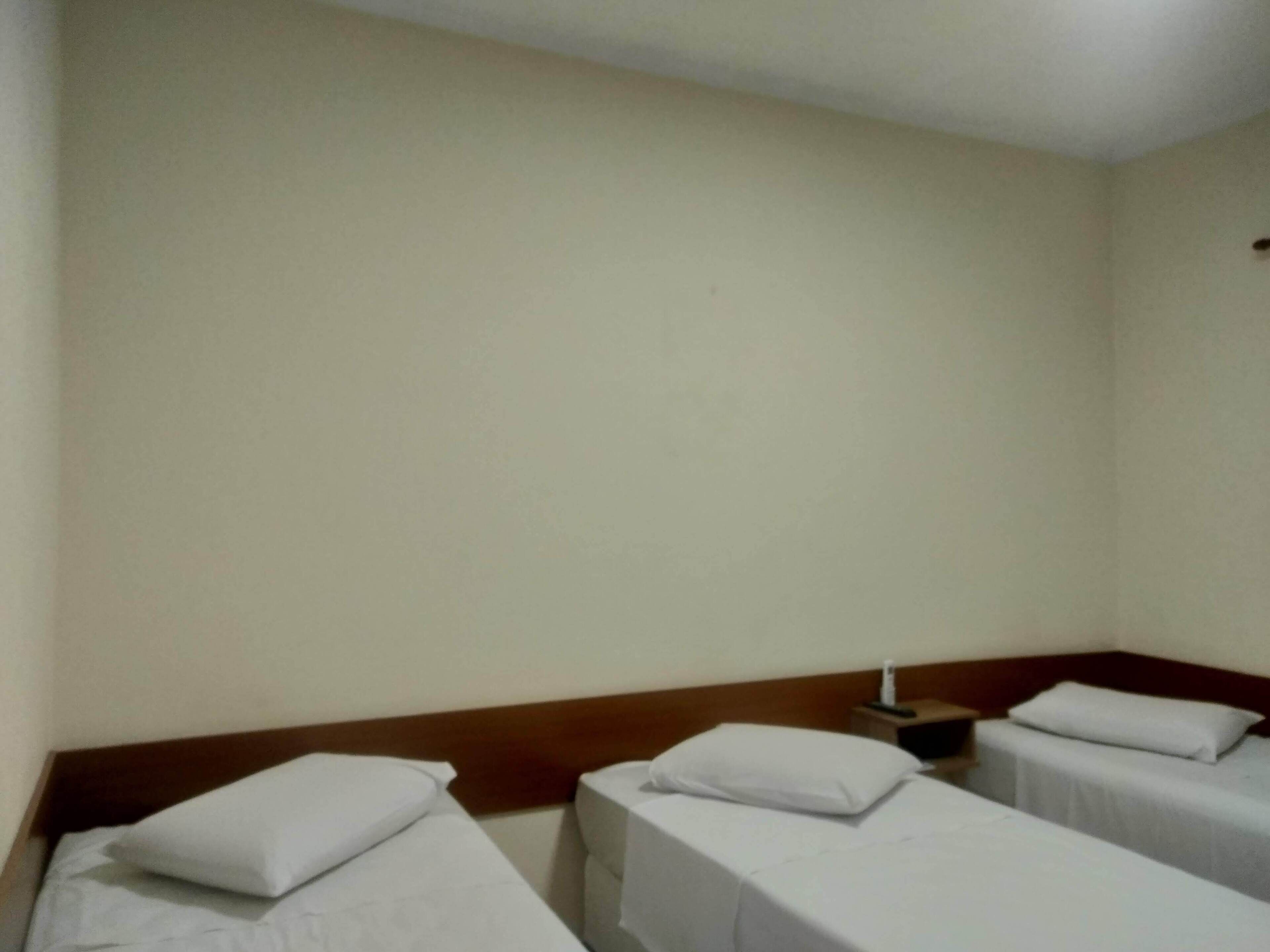 Habitación de hotel con dos camas individuales, cada una con una almohada blanca y un cabecero de madera.
