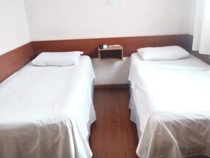 A small, clean room with two single beds, a nightstand, and a wooden headboard. - Lelis Hotel (Itapira)