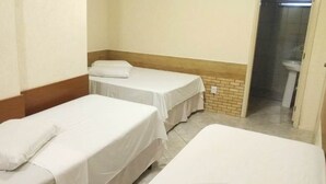 Una habitación con dos camas individuales, cada una con una almohada y una colcha blanca. Hay un panel de madera a lo largo de la pared inferior, y se ve un baño a través de una puerta abierta.