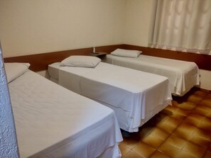 A hotel room with three single beds, each with white bedding and pillows. The room has a tiled floor and a wooden headboard. - Lelis Hotel (Itapira)