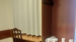 Una habitación de hotel con un escritorio de madera, una silla, un armario y una cama.