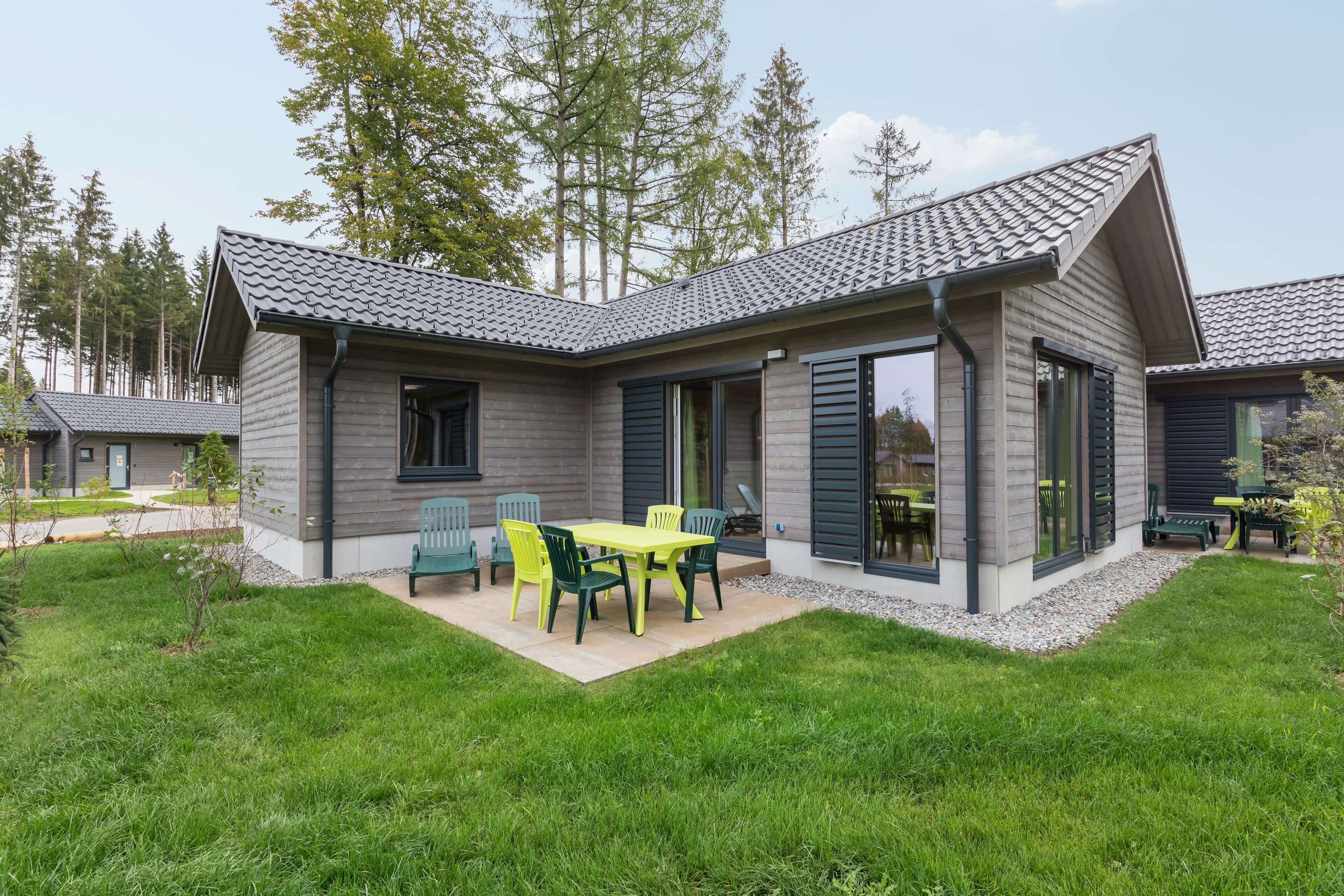 Ein modernes Haus mit überdachter Terrasse, Essbereich mit Stühlen und einem kleinen Garten.