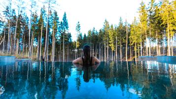 A person in a swimming pool surrounded by tall trees.