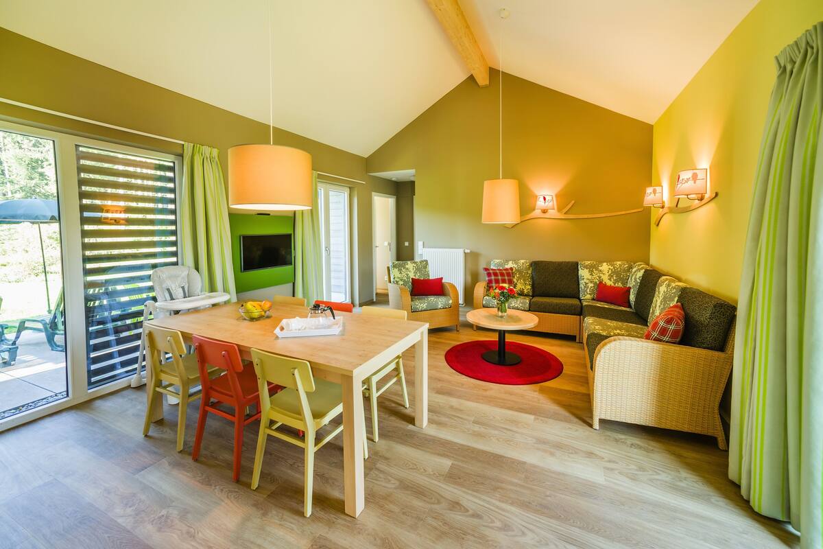 A spacious living area with a wooden dining table, colorful chairs, a sofa, and a small coffee table.