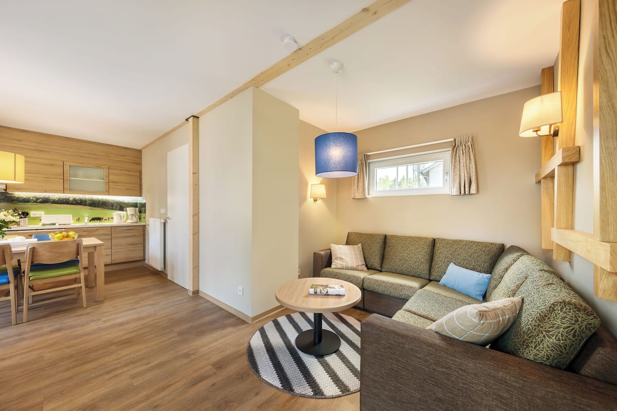 A modern living room with a wooden floor, a round coffee table, a sofa with patterned cushions, and a dining area with a wooden table and chairs.
