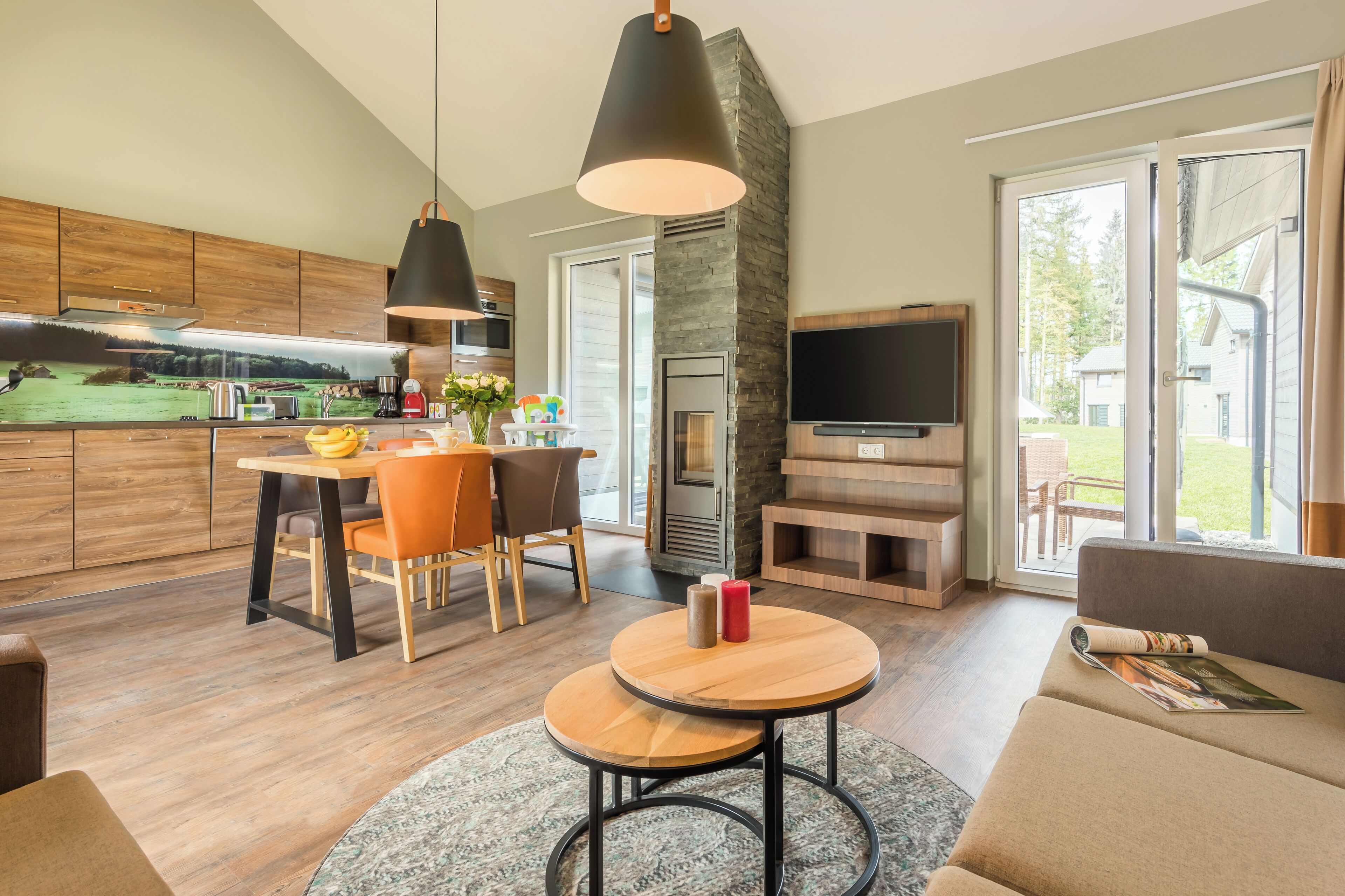 Eine moderne Küche mit Holzausbau, einer Essecke mit orangefarbenen Stühlen, einem runden Holztisch und einem Kamin aus Stein.
