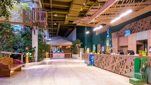 A reception area with a wooden reception desk, a seating area with benches, and a green wall with a decorative figure. - Center Parcs Bungalowpark Allgäu (Leutkirch im Allgau)