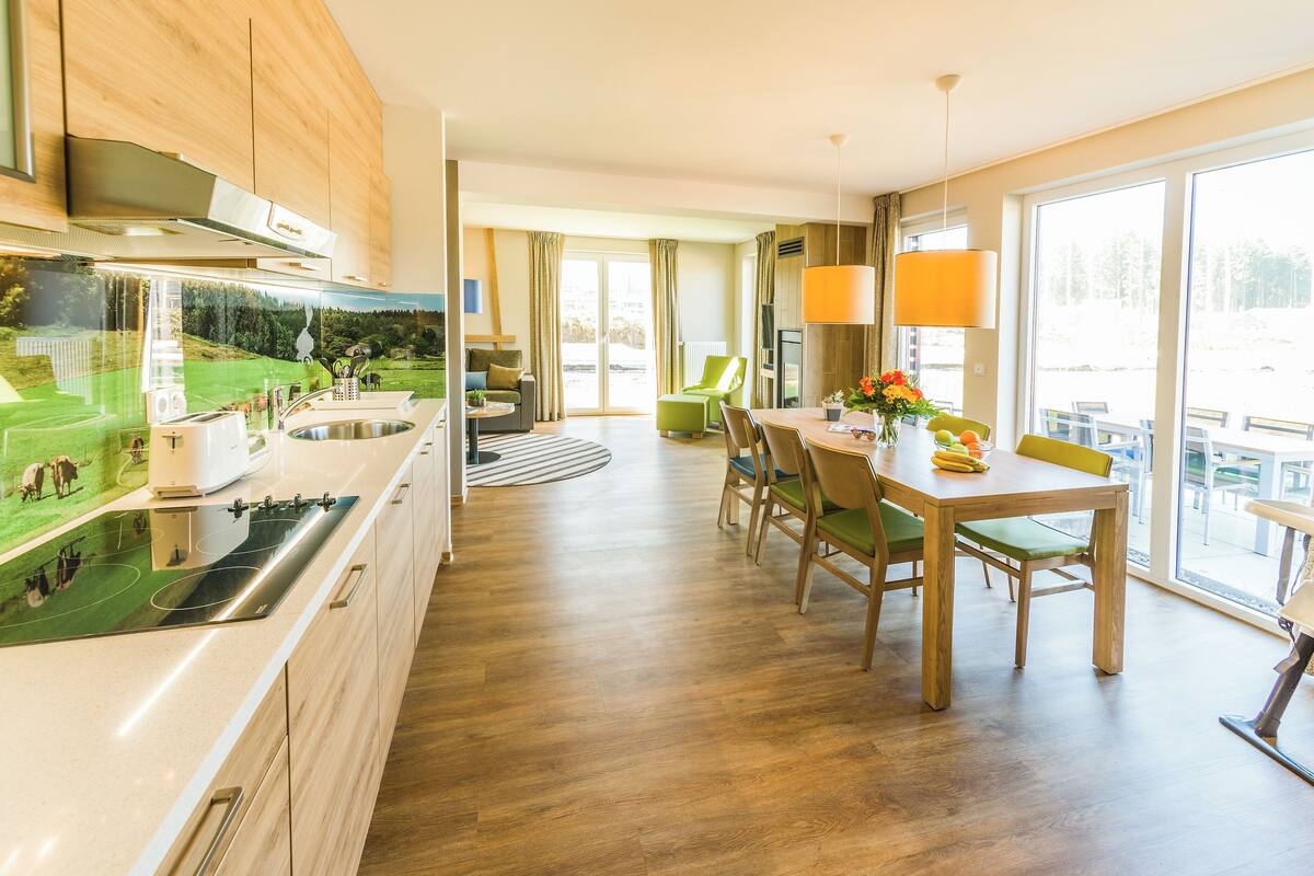A modern kitchen with wooden cabinets, a built-in stove, and a large window overlooking a scenic landscape.