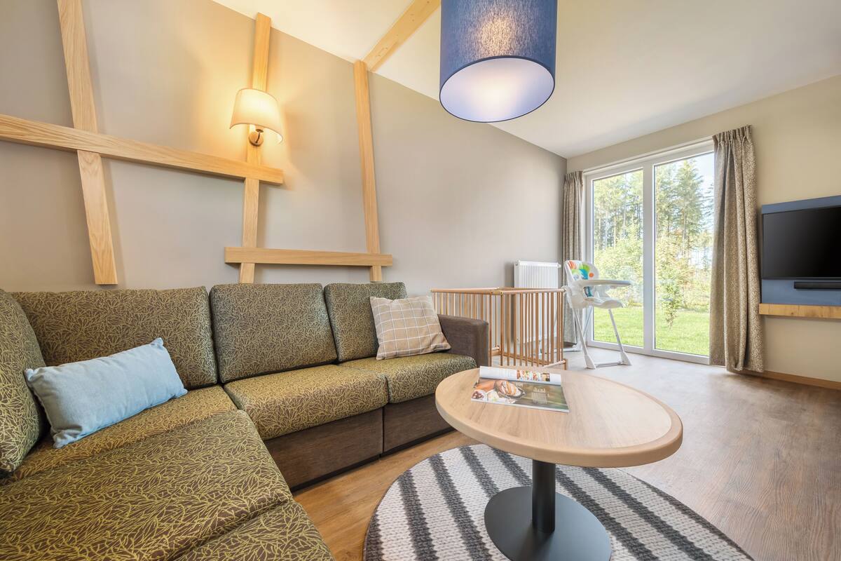 A modern living room with a sectional sofa, a round coffee table, a TV, and a large window with curtains.