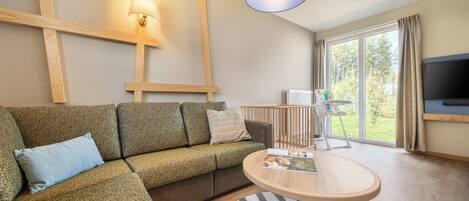 A modern living room with a sectional sofa, a round coffee table, a TV, and a large window with curtains.