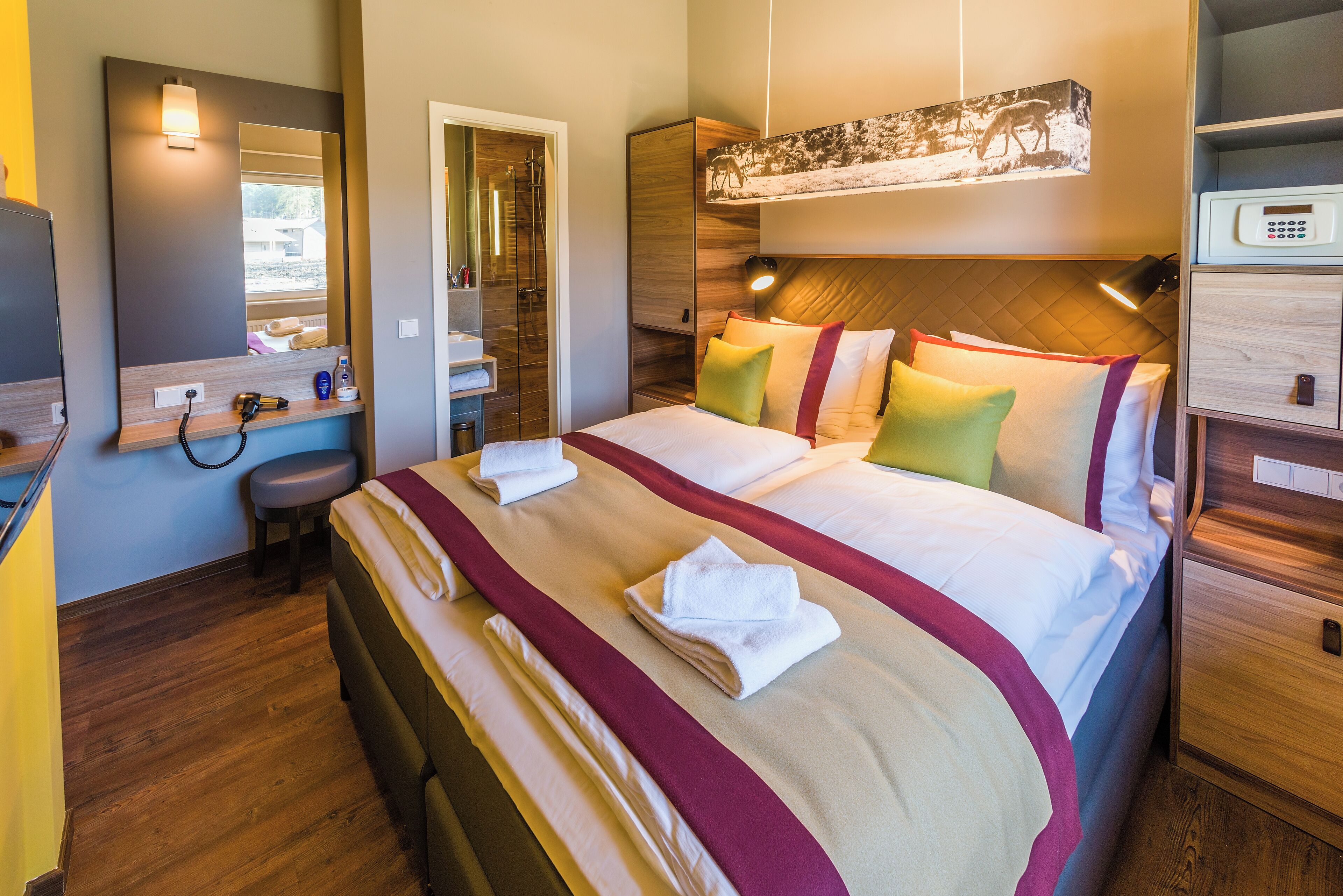 Ein Hotelzimmer mit einem großen Bett, einem Nachttisch, einem Spiegel, einem Kleiderschrank und einem Duschbereich.