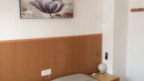Ein Schlafzimmer mit einem hölzernen Kopfteil, einem Bett mit grauer Bettdecke, einem Nachttisch mit Lampe und einem Bild an der Wand.