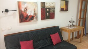 Ein modernes Wohnzimmer mit einem schwarzen Sofa, zwei roten Kissen und drei abstrakten Bildern an der Wand.