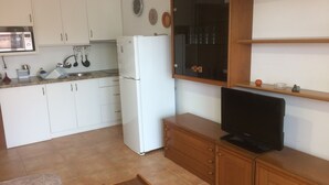 Eine kleine Küche mit weißen Schränken, einem weißen Kühlschrank, einer Mikrowelle und einem Holzschrank mit Fernseher.