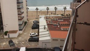 Blick auf einen Parkplatz mit mehreren Autos, einen Strand mit Palmen und ein Gebäude mit Balkonen mit Meerblick.