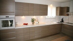 A modern kitchen with wooden cabinets, a built-in oven, a sink, and a countertop with a plant and a coffee machine.
