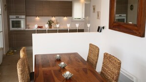 A modern kitchen with wooden cabinets, a built-in oven, and a dining area with a wooden table and wicker chairs.