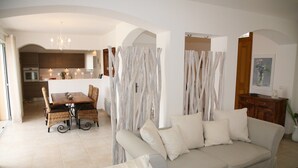 A living room with a sofa, a dining table with chairs, and a kitchen in the background.